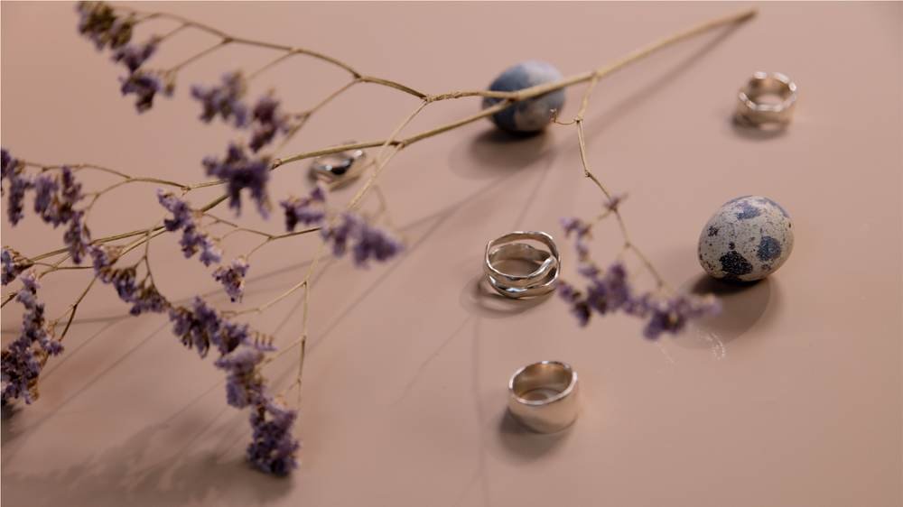 Silver rings and dried lavender scattered across a warm blush surface