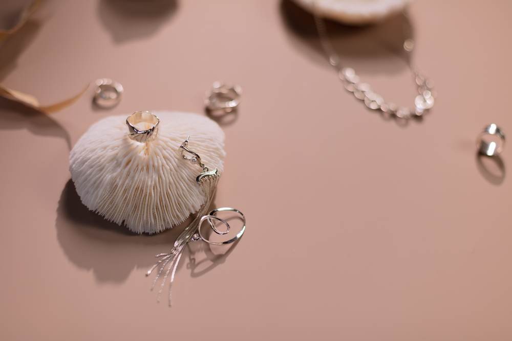 Silver rings and a crystal drop necklace arranged with a white shell on a warm terracotta surface