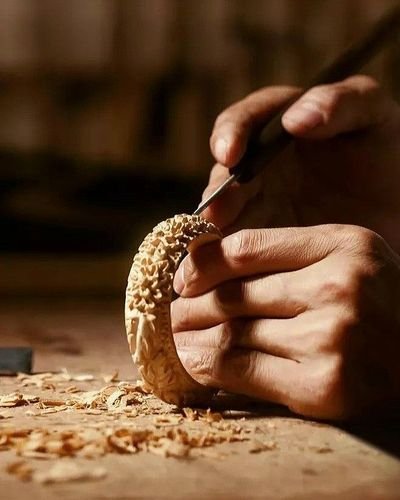 Hands carving openwork detail into a small wooden piece, shavings across the bench