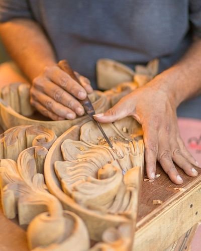 An artisan shaping deep scroll and leaf relief across a wooden panel