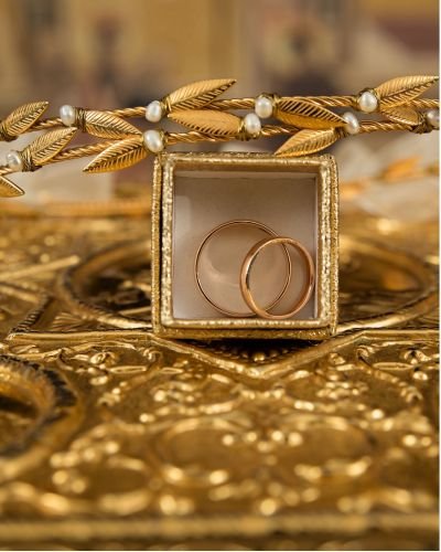 Gold wedding bands in a jewellery box, beneath a pearl-detailed gold chain