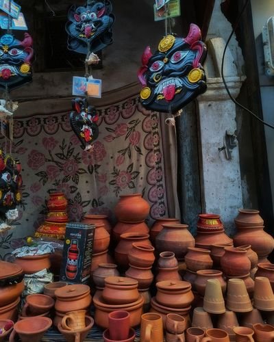 Terracotta pots and lidded vessels below painted ritual masks