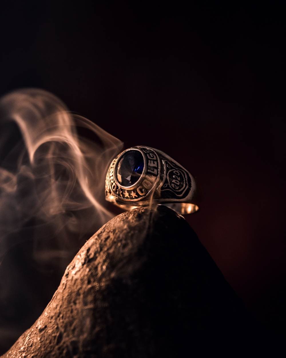 A gold ring set with a deep blue stone, lit against dark, smoke-filled surroundings