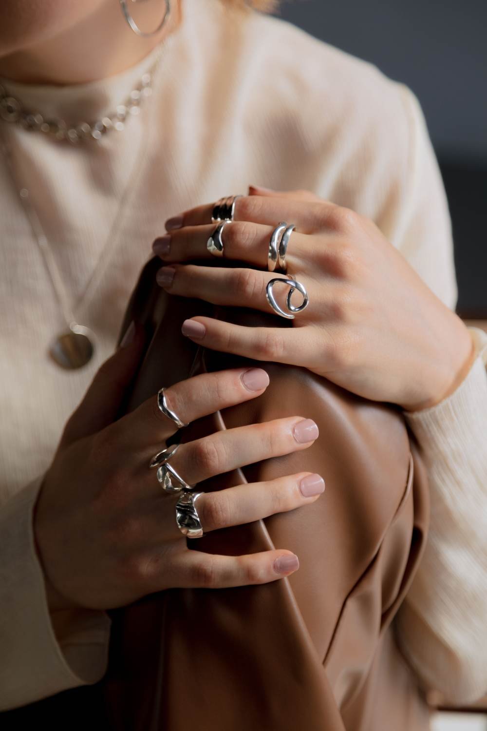 Hands wearing stacked silver rings and a fine pendant necklace