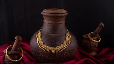 A gold necklace draped over a terracotta pot beside a gold bangle
